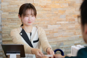あゆみ歯科クリニックの女性受付スタッフが患者へ診察券を渡しているところ