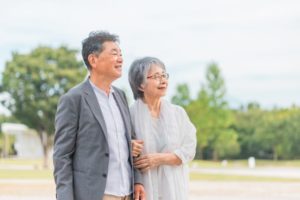 屋外で寄り添う白髪まじりの老夫婦。